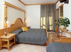 Een slaapkamer met een houten bed, nachtkastje, dressoir, spiegel en een potplant.
