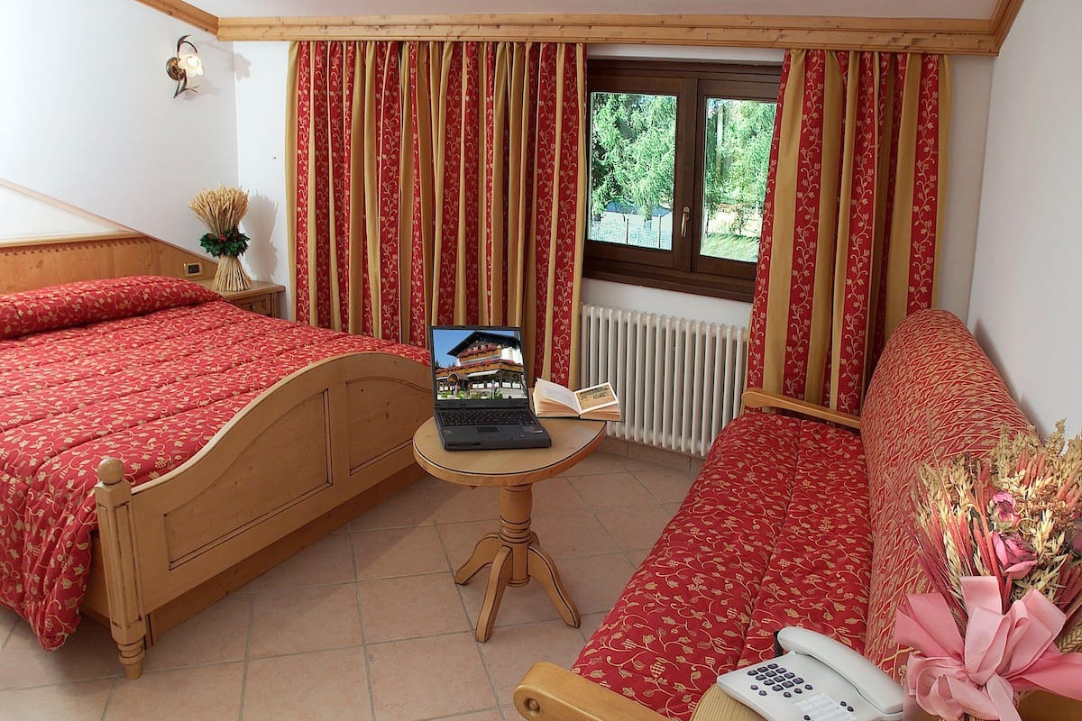 Quarto com duas camas, uma mesinha de apoio com um laptop e um livro, telefone ao lado da cama e uma janela com cortinas.