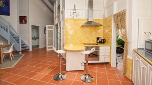 Een keuken met een gele betegelde spatwand, een rvs afzuigkap en een klein eiland met barkrukken.