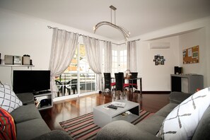 Una sala de estar moderna con un televisor de pantalla plana, sofás grises, una mesa de centro y un comedor con sillas y una mesa.