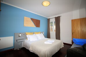 Un dormitorio con cama, mesita de noche, luz de pared, ventana con cortinas y puerta de madera.