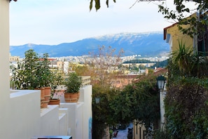 Una calle estrecha con macetas de terracota en los balcones, una farola y una vista de la ciudad y las montañas al fondo.
