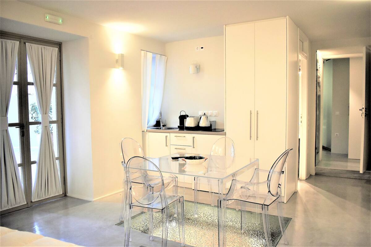 A modern kitchen with a glass dining table and chairs, a white cabinet, and a window with curtains.