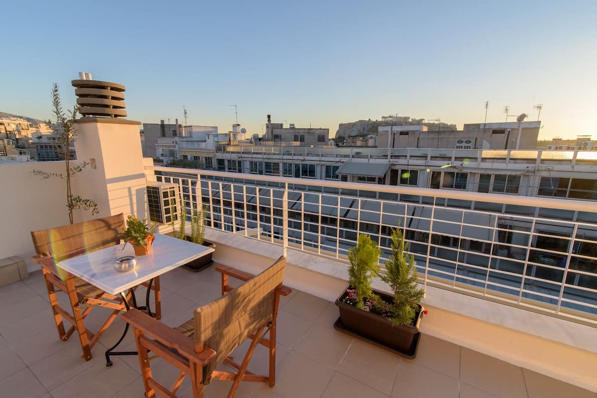 A rooftop terrace with a table and chairs, potted plants, and a view of the cityscape.
