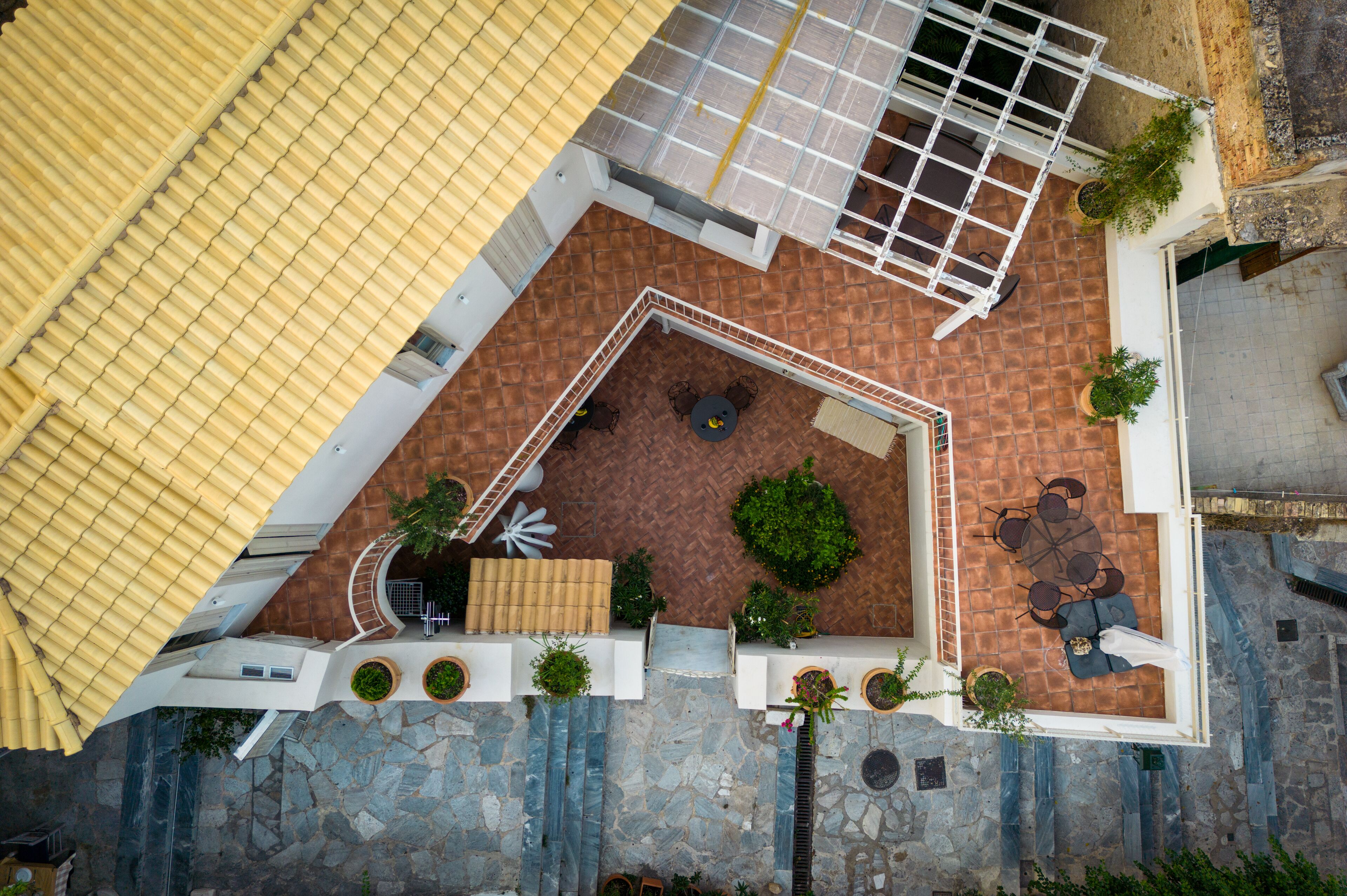 An aerial view of a courtyard with a tiled floor, surrounded by walls and potted plants.