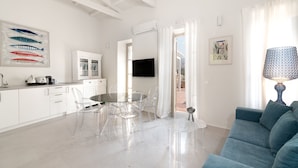 A modern living room with a blue sofa, a glass dining table with chairs, a TV, and artwork on the walls. - Acropolis Suites (Athens)
