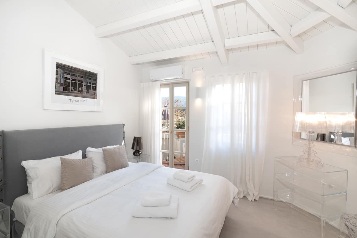 A modern bedroom with a large bed, a bedside table, a clear glass dresser, and a framed picture on the wall.