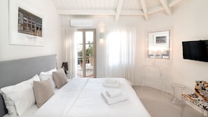 A hotel room with a large bed, a TV, a clear glass table, and a balcony with a view. - Acropolis Suites (Athens)