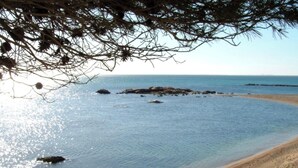 Une scène de plage avec une eau claire, un rivage sablonneux et des affleurements rocheux.