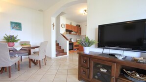 Ein Wohnzimmer mit großem Flachbildfernseher, Holzmöbeln und einer Treppe, die zur Küche führt.