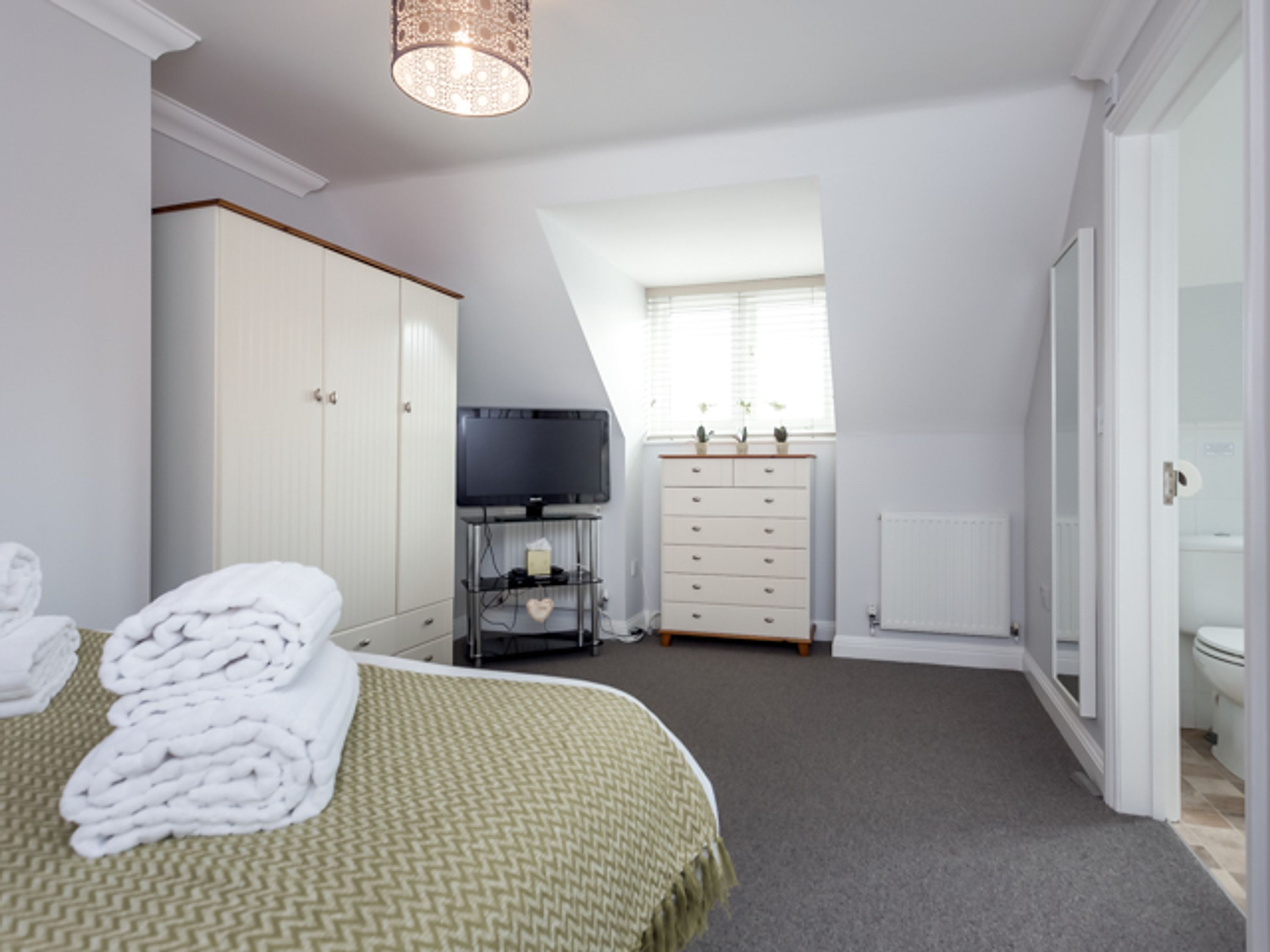 Un dormitorio con cama, televisión, cómoda y ventana.