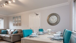A dining area with a wooden table set for four, teal chairs, and a wall clock. - Angel Mews (Poole)