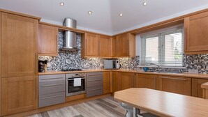 A modern kitchen with wooden cabinets, a built-in oven, a microwave, and a window with blinds. - Angel Mews (Poole)