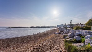 A pebbled beach with a rocky breakwater, a clear sky, and distant industrial structures. - Ammonite (Poole)