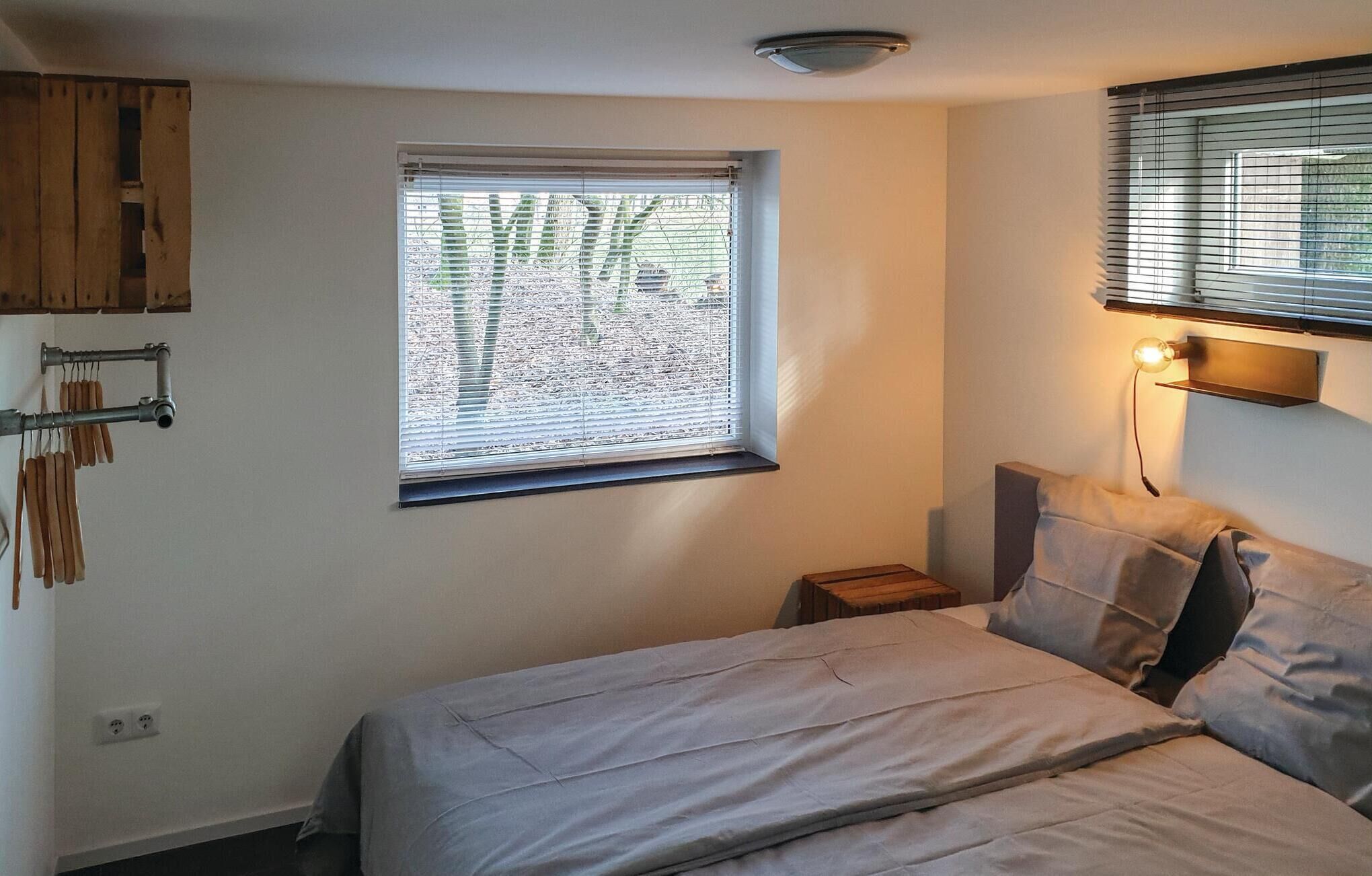 A bedroom with a bed, a window with blinds, a bedside lamp, and a wall-mounted shelf.