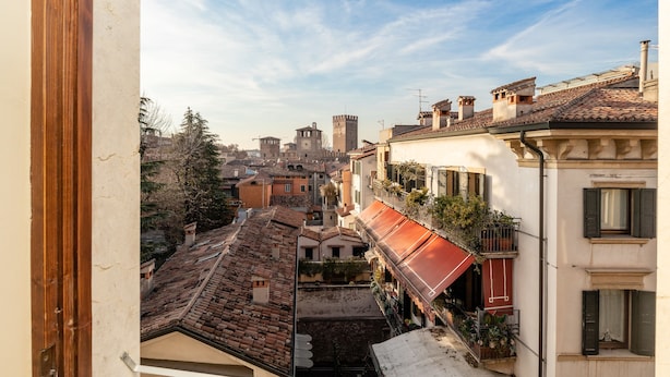 A view from a balcony overlooking a historic town with traditional architecture, including a prominent tower and terracotta-roofed buildings. - Scaligerorooms (Verona)