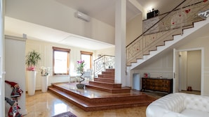 A spacious living area with a marble floor, a white leather sofa, a staircase with ornate railings, and a potted plant. - Scaligerorooms (Verona)