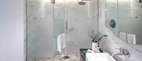 Une salle de bain moderne dotée d’une douche à parois de verre, d’un sol carrelé en marbre, d’un lavabo avec un plan de toilette en marbre et d’un grand miroir.