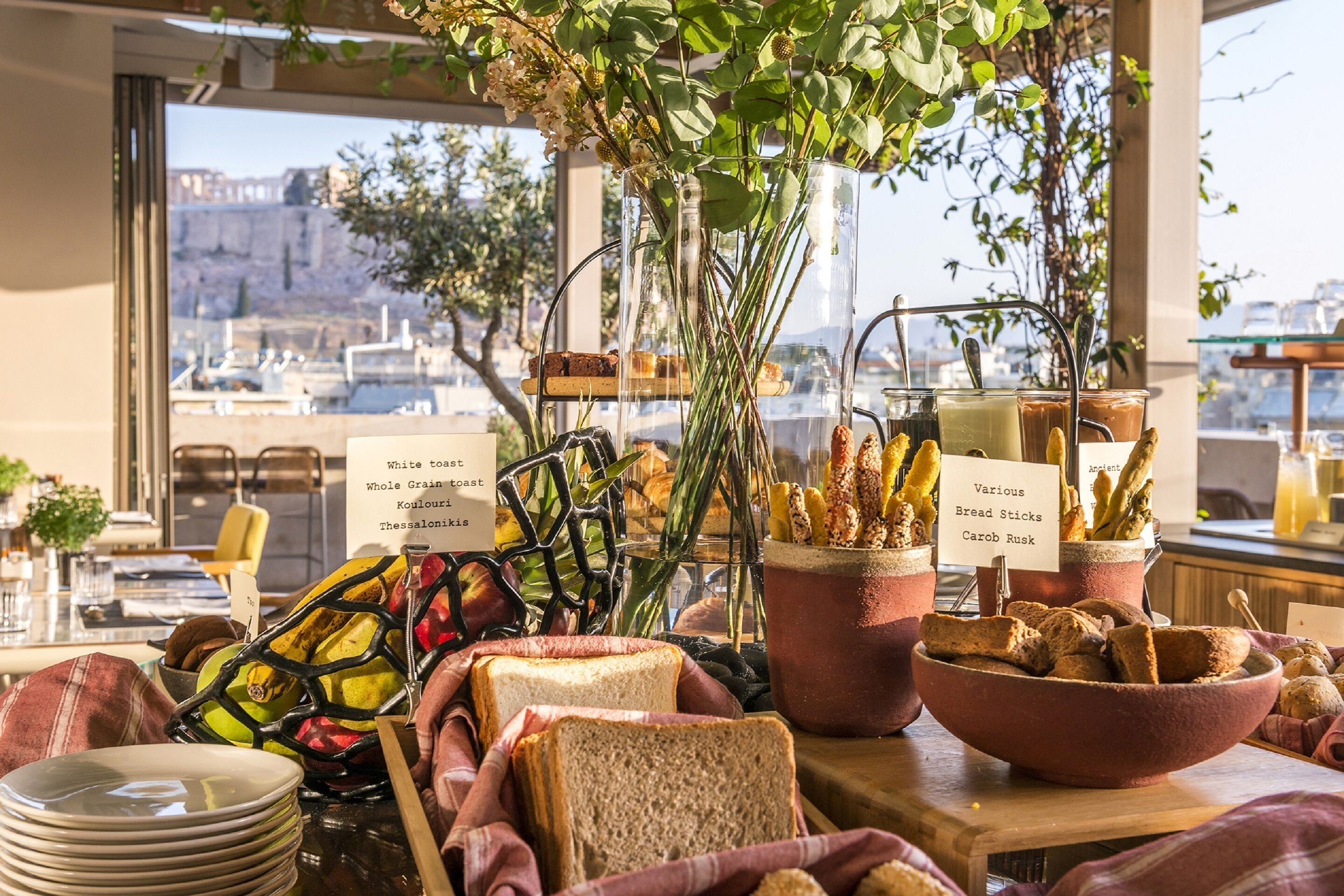 A breakfast buffet with various bread and toast options, a view of the city through large windows, and a rustic interior design.