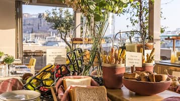 Een ontbijtbuffet met diverse soorten brood en toast, een uitzicht over de stad door grote ramen, en een rustiek interieur.