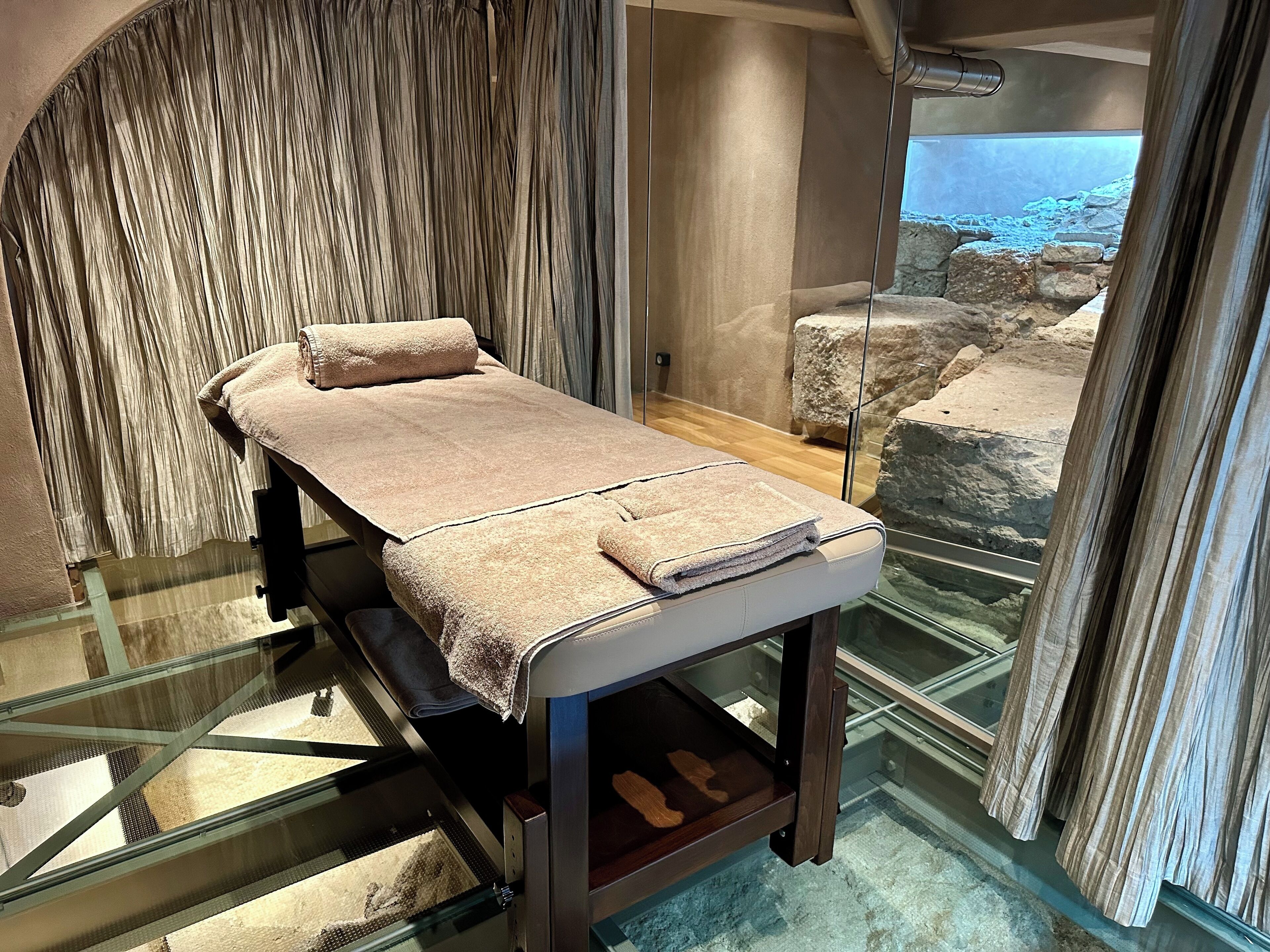 En massagebänk med handdukar, glaspaneler och utsikt över klippor och vatten.