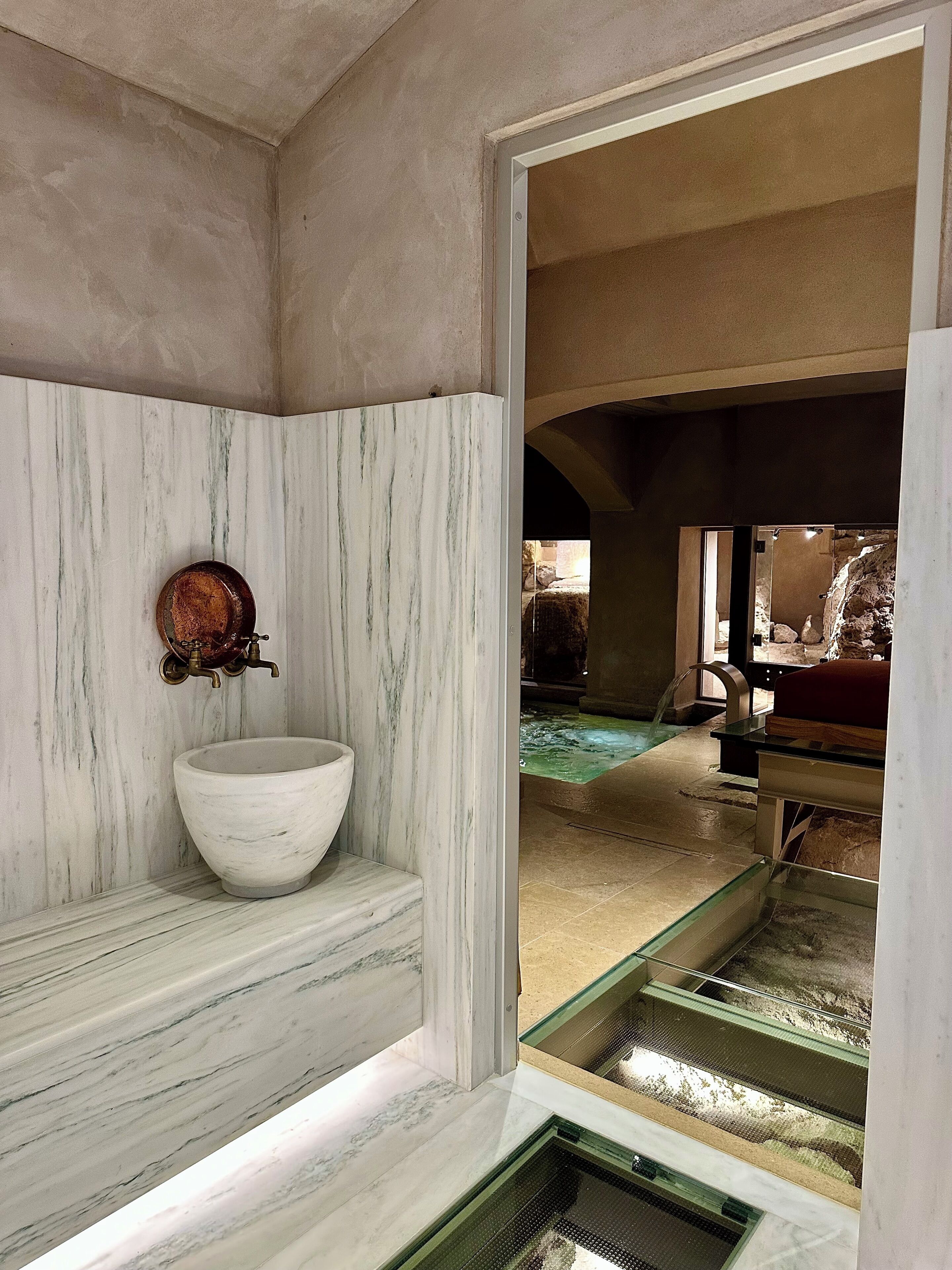 A bathroom with a marble sink, a vintage faucet, and a glass-enclosed spa area.