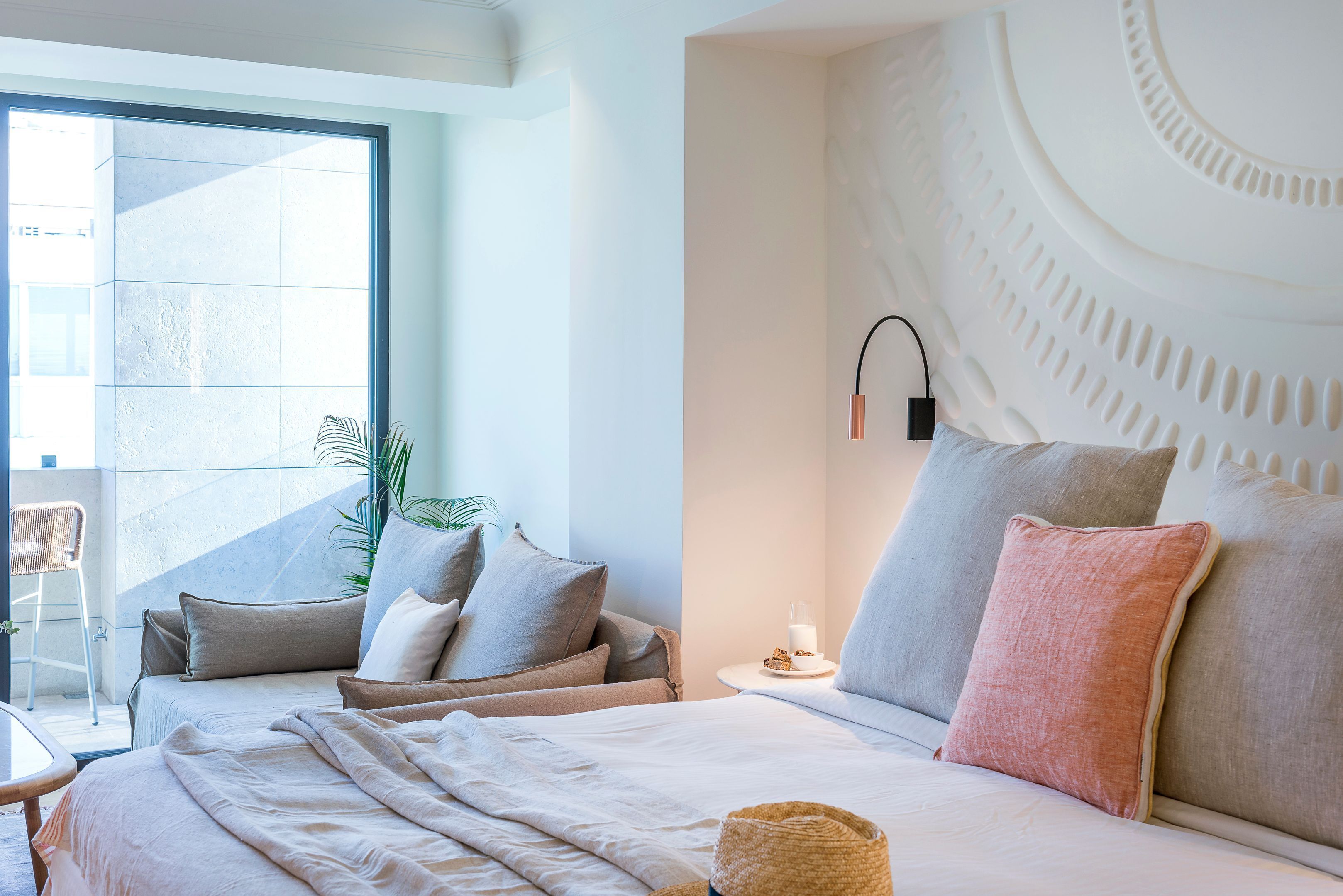 Un hotel moderno con una cama grande, una mesita de noche, una lámpara de pared y vistas amplias por una ventana grande.