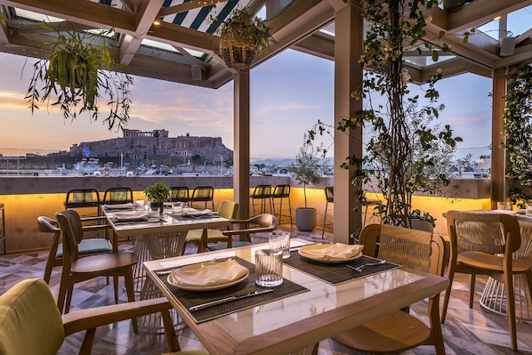 Ein Restaurant mit gedeckten Tischen, Blick auf ein historisches Gebäude und hängenden Pflanzen.