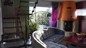 Ein modernes Wohnzimmer mit einer gebogenen Couch, einem Kamin, einer Wendeltreppe und Blick ins Grüne.