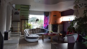 Ein modernes Wohnzimmer mit Ecksofa, Couchtisch und Kamin. Eine Treppe führt auf eine obere Ebene, und das Zimmer hat große Fenster.