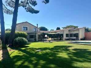 Ein zweistöckiges Haus mit Naturstein-Fassade, einer überdachten Terrasse und einem Swimmingpool.