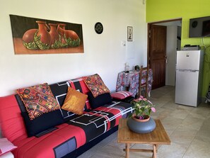 Uma sala de estar com um sofá, uma mesa com uma planta, um relógio e uma televisão.