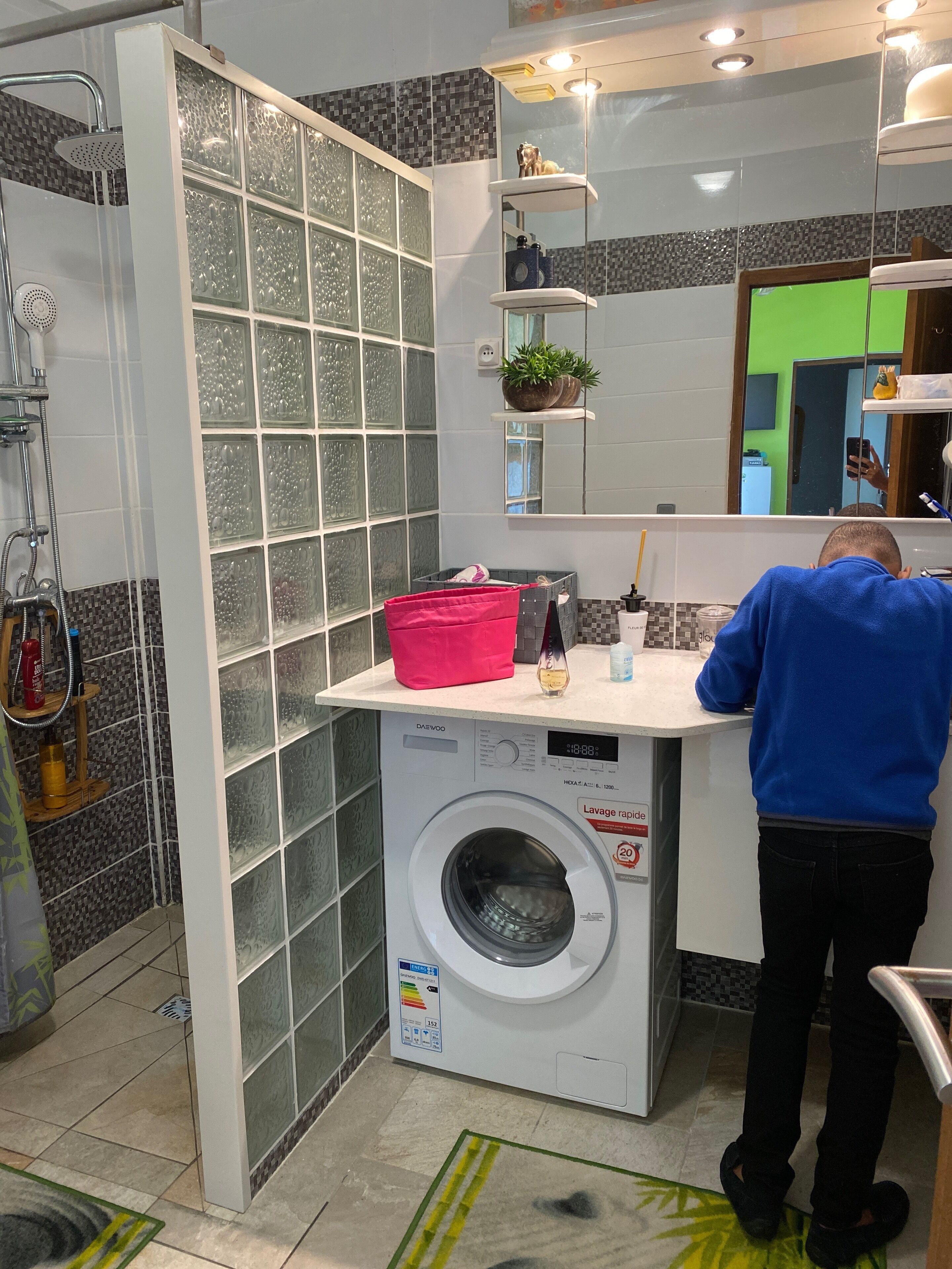A bathroom with a glass shower enclosure, a built-in washing machine, and a mirror with a green-tinted section.