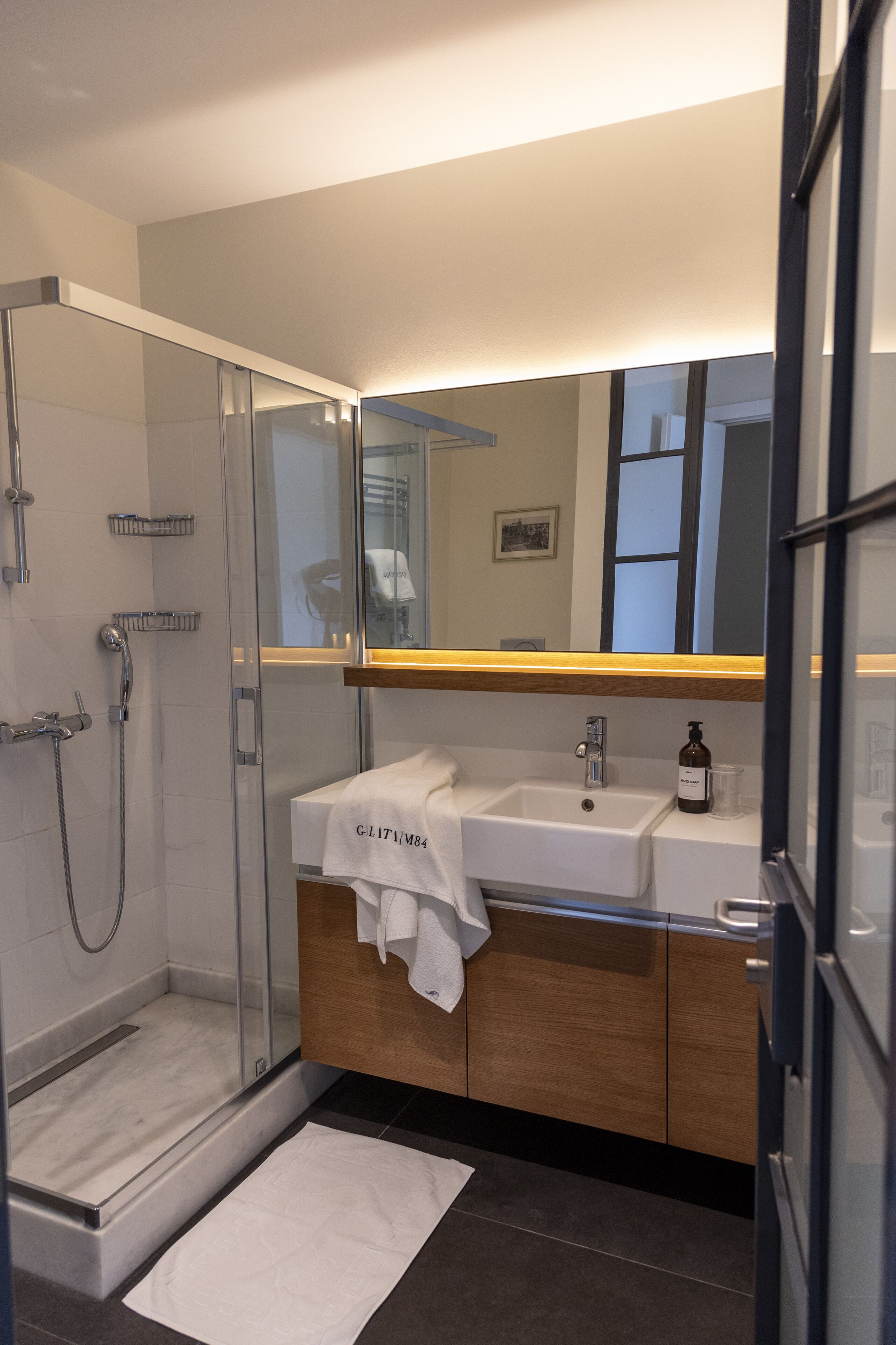 Un baño moderno con cabina de ducha de vidrio, un lavamanos blanco con una toalla y un mueble de tocador de madera.