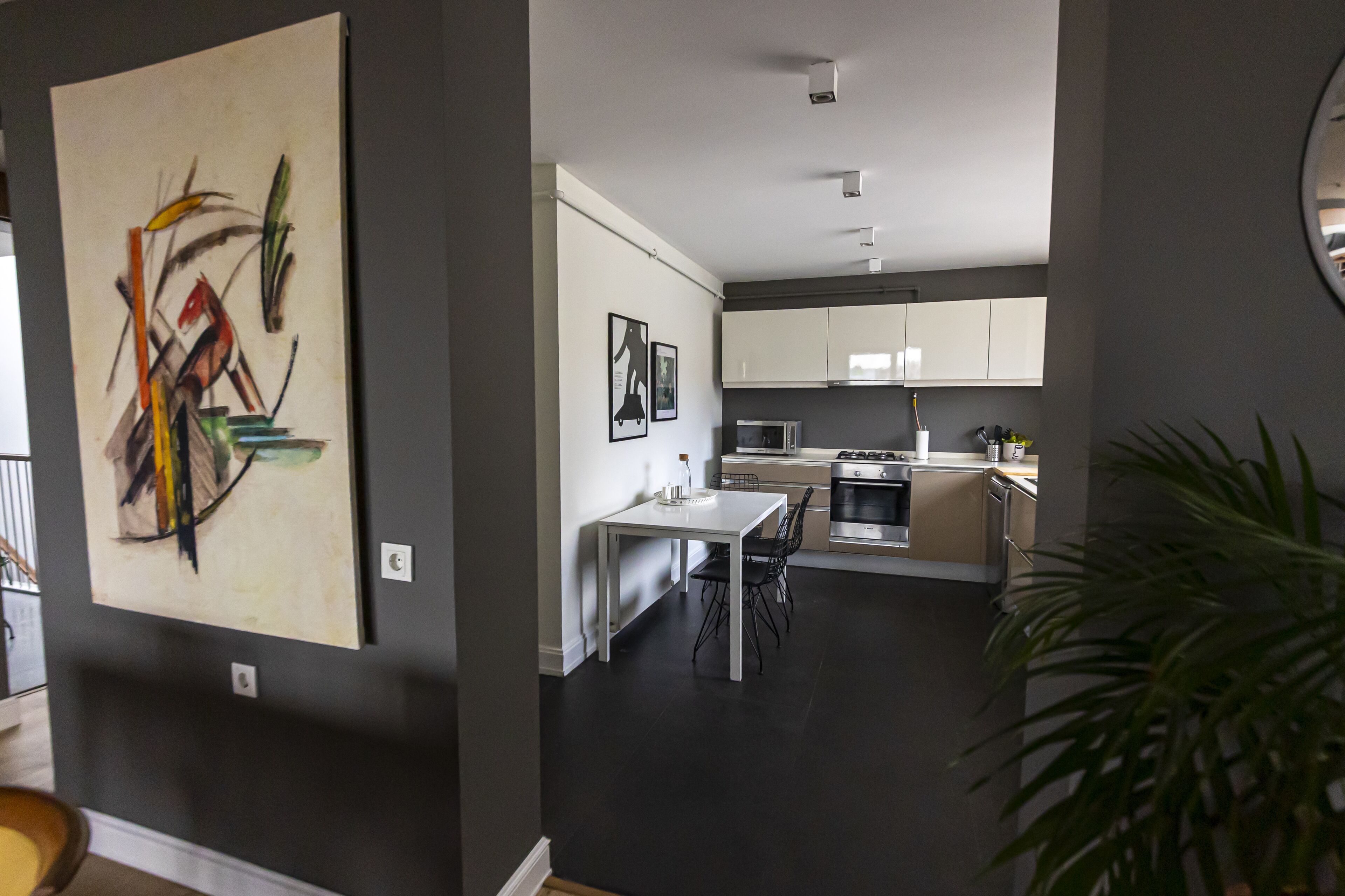 Een moderne keuken met witte kasten, een eettafel en stoelen. Aan de muur hangt een groot abstract schilderij.