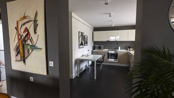 Een moderne keuken met witte kasten, een eettafel en stoelen. Aan de muur hangt een groot abstract schilderij.