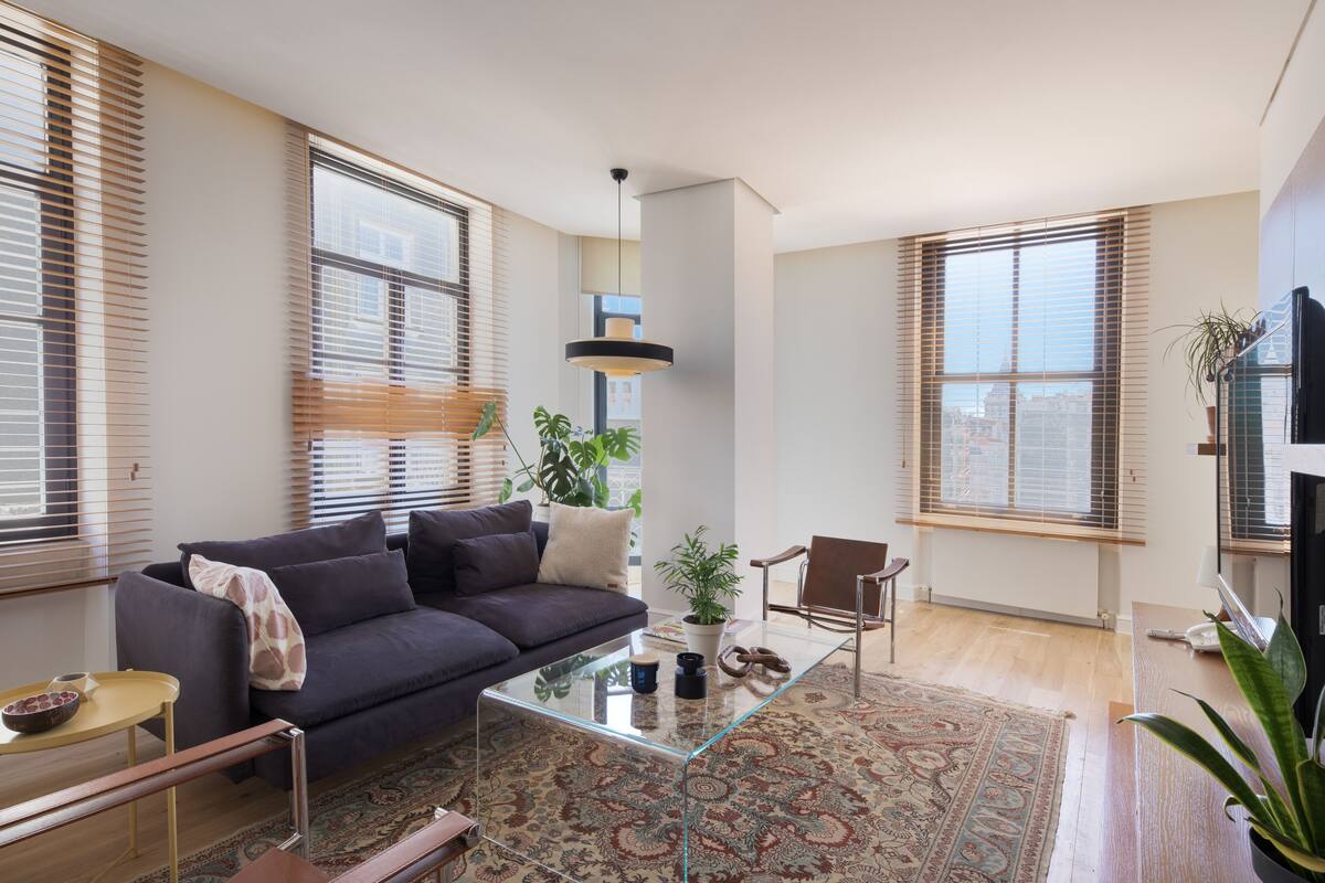 A modern living room with a dark grey sofa, a glass coffee table, and a patterned rug.