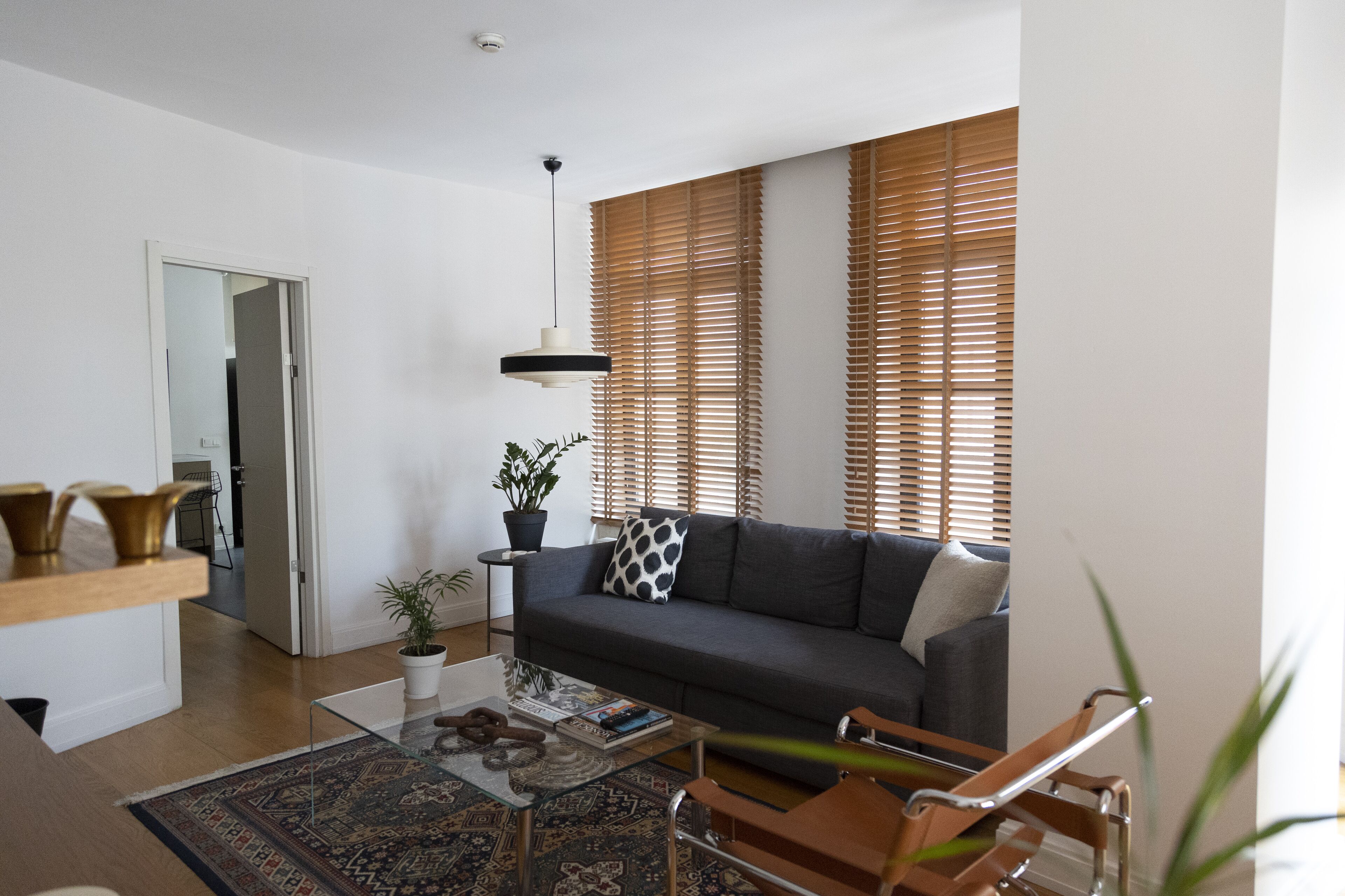 A modern living room with a sofa, coffee table, and a glass-top table. There is a potted plant and a wooden bench.
