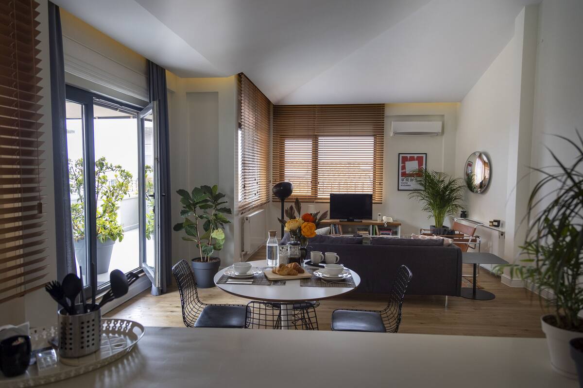 A modern living space with a dining area, a sofa, a TV, and potted plants.