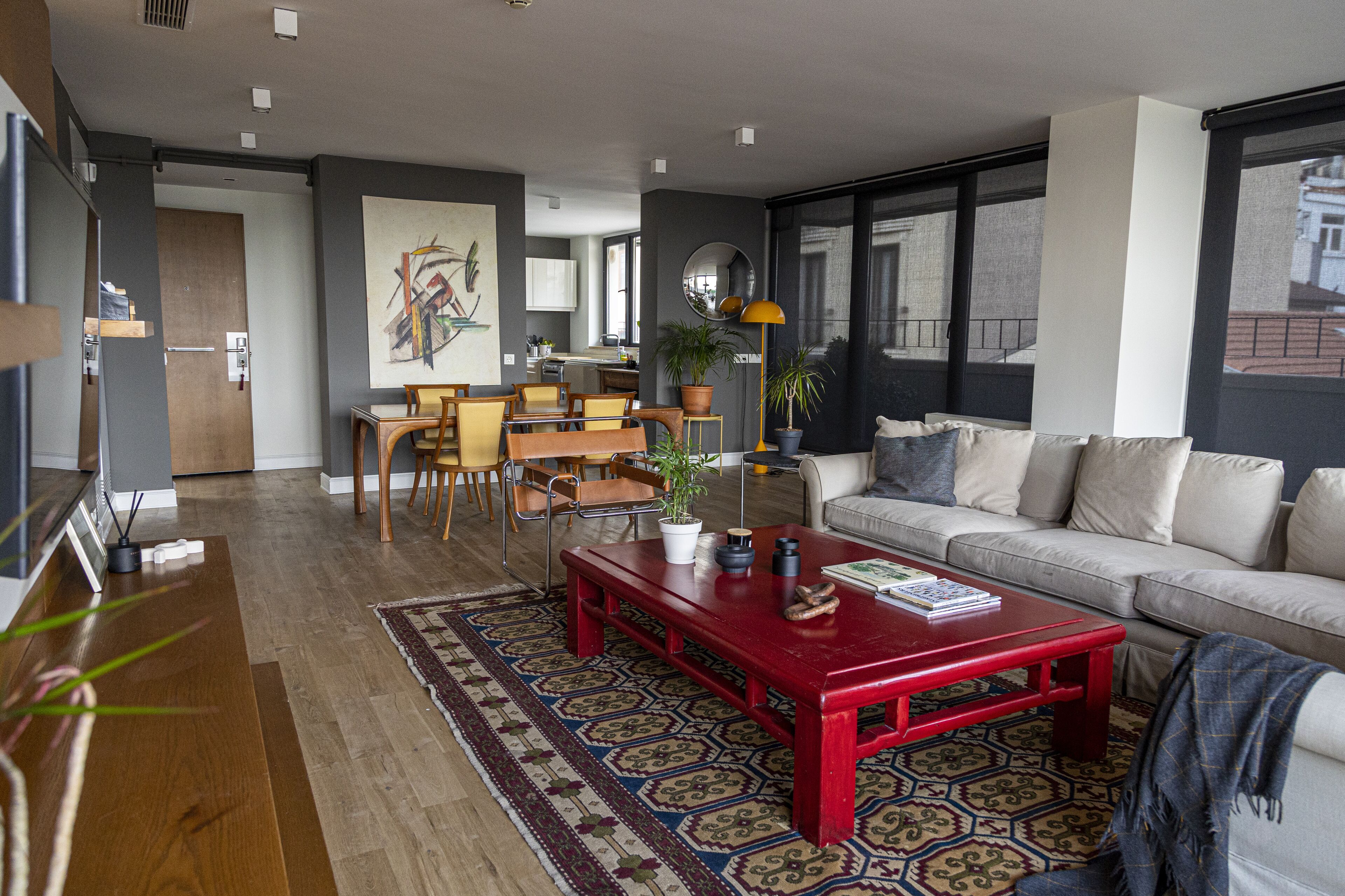 A modern living room with a red coffee table, a sofa, and a dining area with chairs and a table.