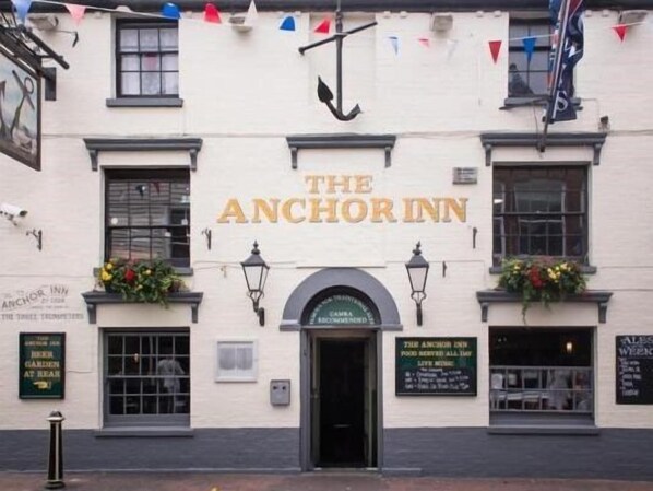 The exterior of The Anchor Inn, featuring a traditional facade with a prominent sign, windows, and flower boxes.