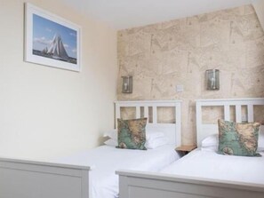 A room with two single beds, each with a headboard and a pillow with a map design. There is a framed picture on the wall above the beds.