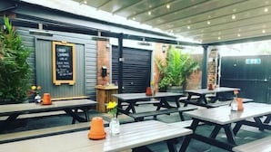 An outdoor patio area with wooden tables and benches, potted plants, and a chalkboard menu. - The Anchor Inn (Cowes)