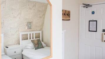 Une chambre avec un mur en pierre, un lit blanc agrémenté d’un coussin décoratif, une table de chevet et une porte avec une pancarte.