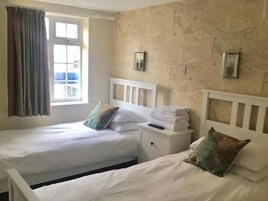 Quarto duplo com duas camas, uma janela com cortinas e um candeeiro fixado na parede.