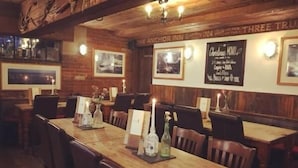 A restaurant with wooden tables and chairs, framed pictures on the walls, and a sign indicating it's The Anchor Inn. - The Anchor Inn (Cowes)
