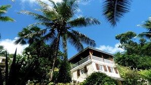 A two-story building with a balcony, surrounded by lush greenery and palm trees.