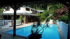 A pool area with a covered patio, potted plants, and a white fence.