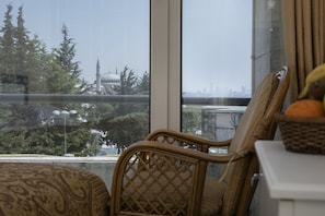 Enjoy a city view from the large window, featuring a prominent mosque in the distance. The room offers a wicker chair, a small table, and a patterned sofa.