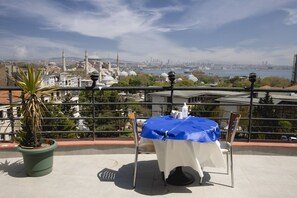 A table with a blue tablecloth on a balcony overlooking a cityscape with a mosque and a river.